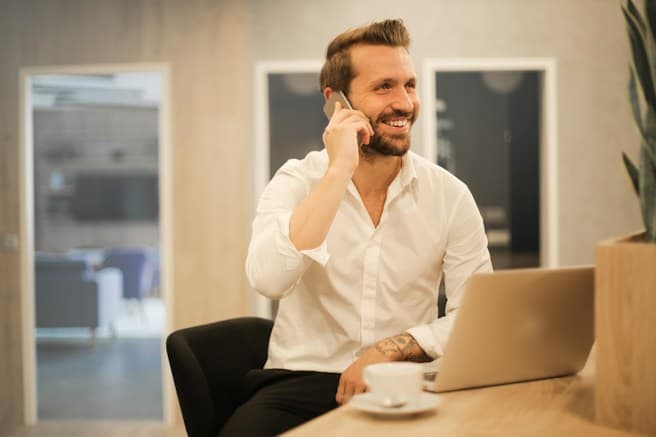 A man smiling while talking on his phone at a desk
